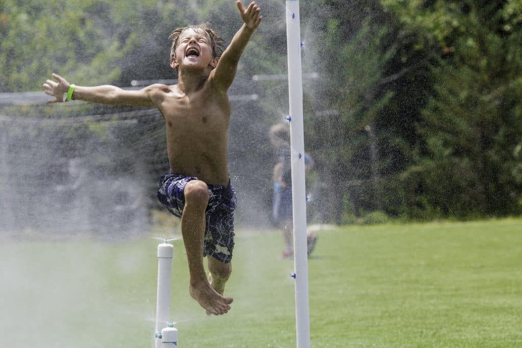 Boy jumping through water sprinklers.
