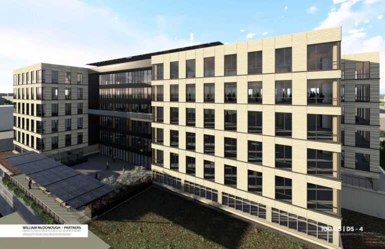 Modern multi-story office building with large glass windows and beige horizontal panels, featuring a central courtyard area with greenery and solar panels on a terrace, set against a partly cloudy sky.