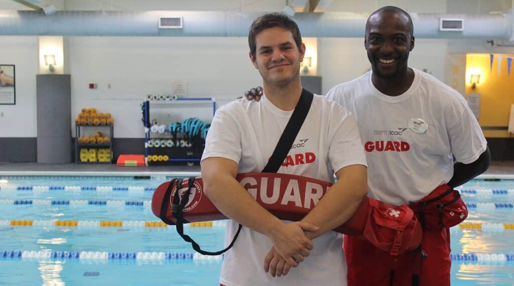 two male lifeguards smiling standing by indoor pool