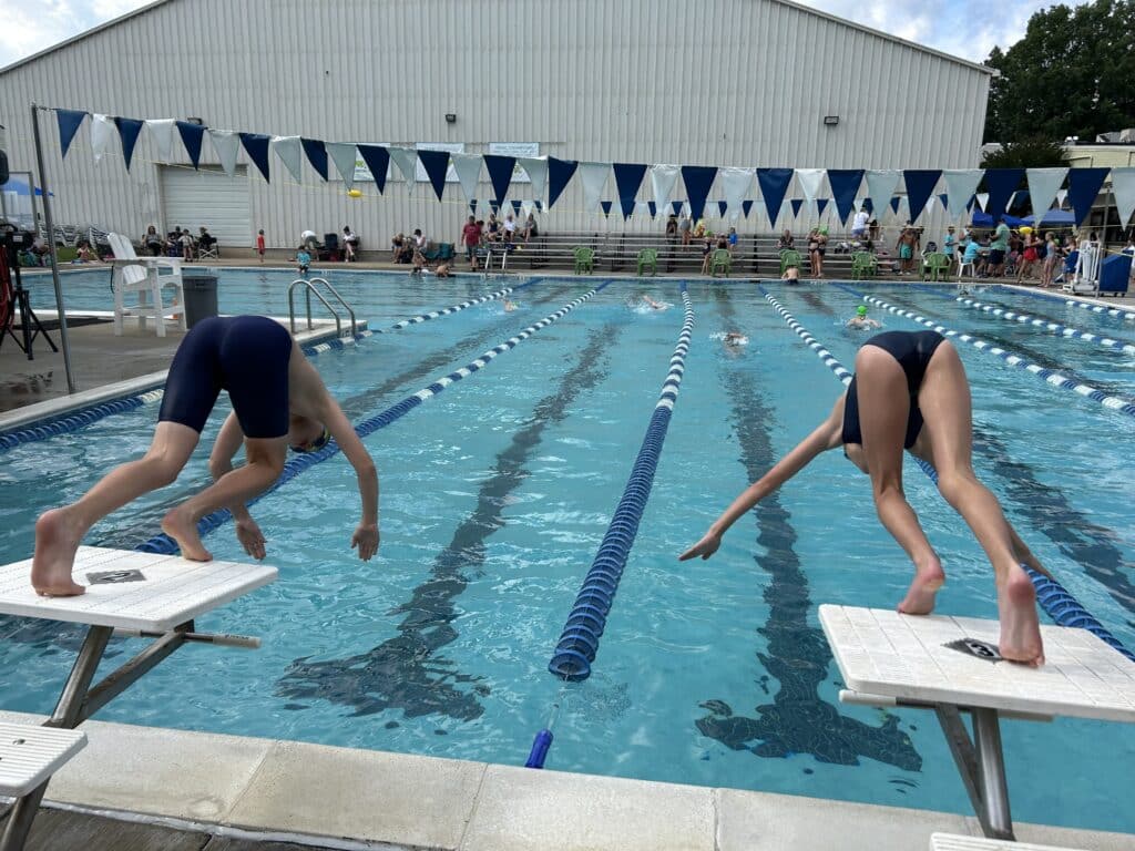 boy and girl swimmers diving off blocks into pool