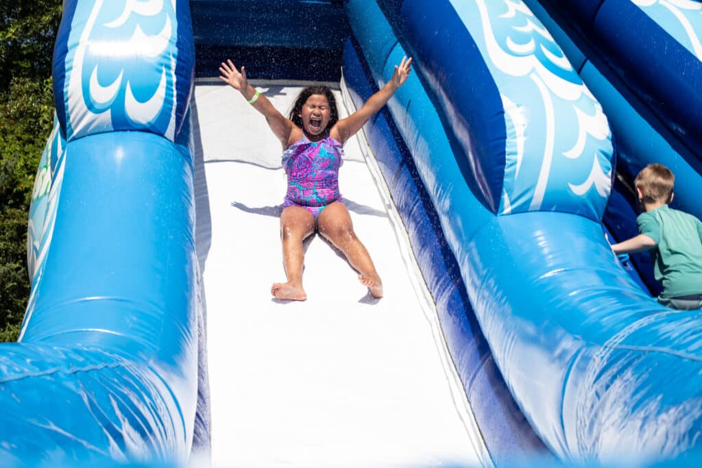 girl going down inflatable slide with arms up