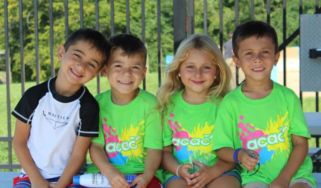 Four kids in green shirts sitting on a picnic table at camp