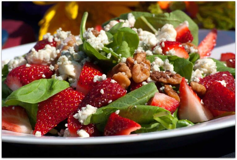 Fresh salad with spinach leaves, sliced strawberries, crumbled feta cheese, and walnuts served on a white plate.