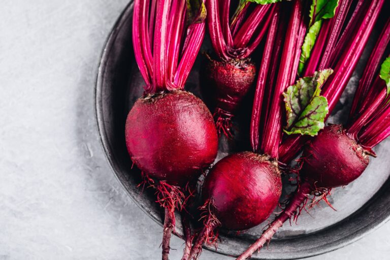 Fresh whole beets with stems and leaves on a dark plate.