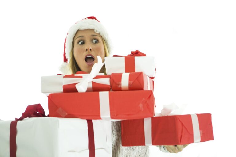Person wearing a Santa hat holding a large stack of wrapped gifts in red and white paper.