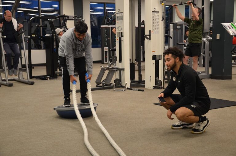 Youth performing battle rope exercises with a trainer in a gym.