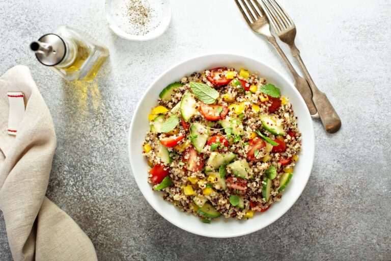 Quinoa salad with chopped vegetables including cucumber, tomato, and bell pepper, garnished with fresh mint leaves in a white bowl.