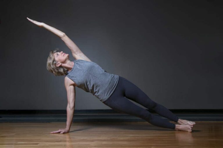 Person performing a side plank exercise on a wooden floor, with one arm extended upward and legs stacked straight.